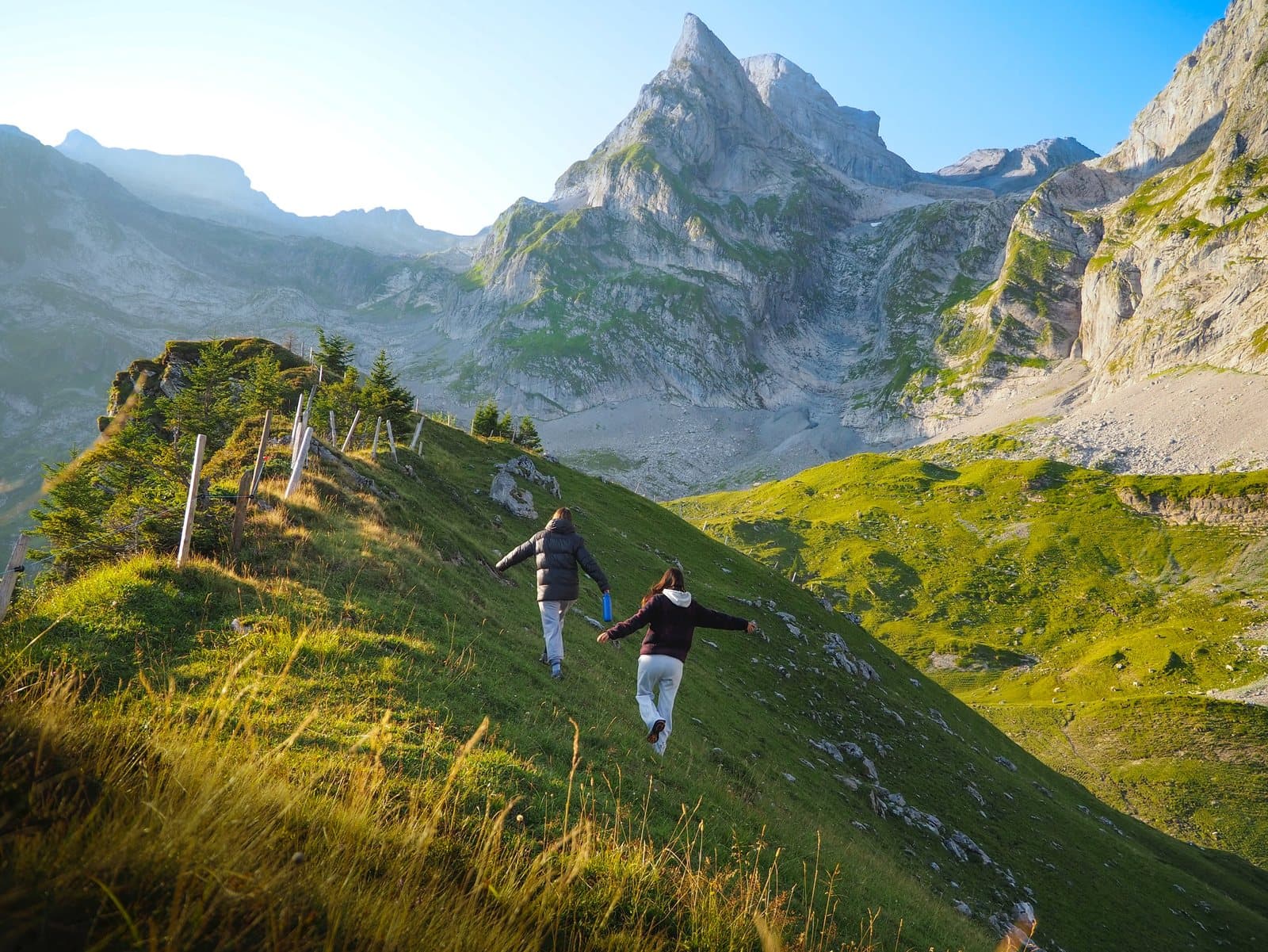 Zwei Wandernde auf dem Weg einen grünen Hang hinauf